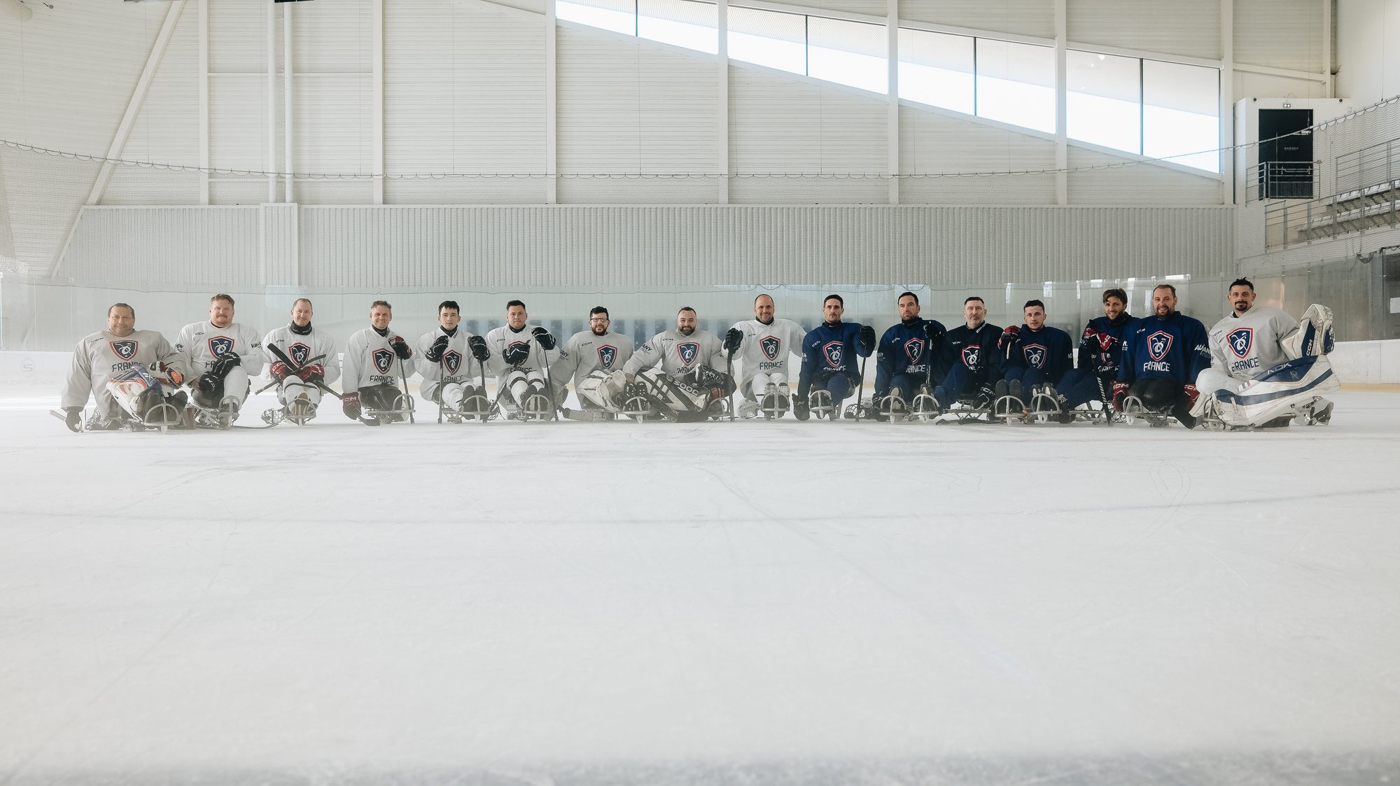 L'équipe de France de para hockey sur glace alignée sur ses luges au milieu de la patinoire, moitié en maillots blancs, moitié en maillots bleus, lors du stage collectif de Cergy-Pontoise