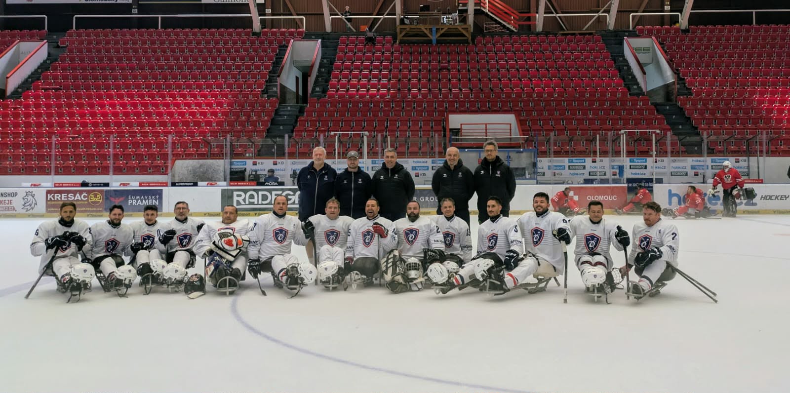 Les joueurs de l'équipe de France alignés sur leurs luges au milieu de la glace, maillots blancs et casques posés devant eux, le staff debout derrière, dans la patinoire aux gradins rouges d'Olomouc